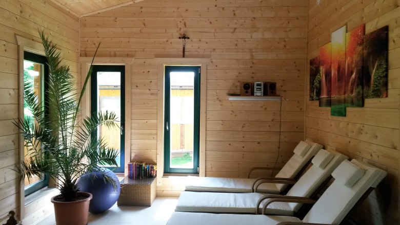 Sauna Hubertushof, © Familie Mies Interior of a sauna with wooden paneling, loungers, a palm tree and a picture on the wall.