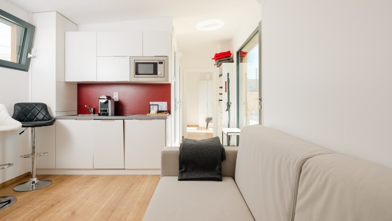 Ipsmiller Apartments, © Michael Reidinger Modern apartment with kitchenette, sofa and bar stool.