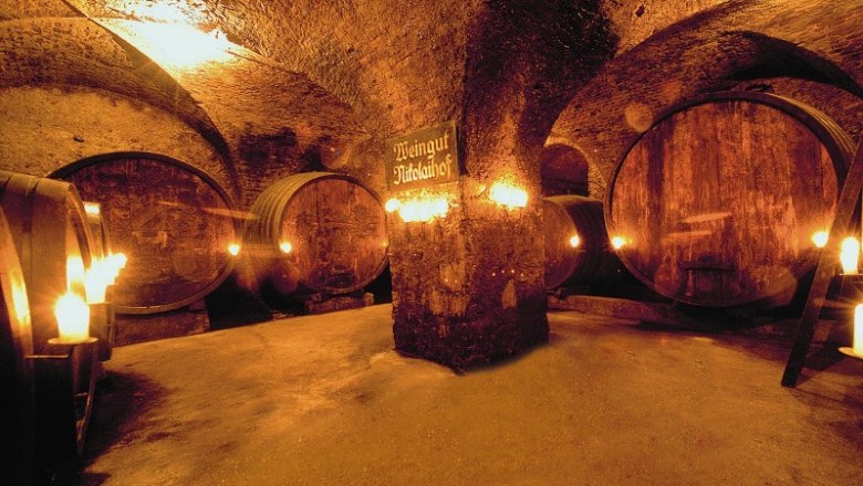 Nikolaihof, © Nikolaihof Historic wine cellar with large wooden barrels and candle lighting.