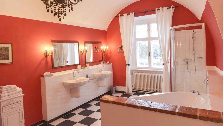 Bathroom, © Schlosshotel Mailberg / point of view Elegant bathroom with red walls, two washbasins, bathtub, shower and chandelier.