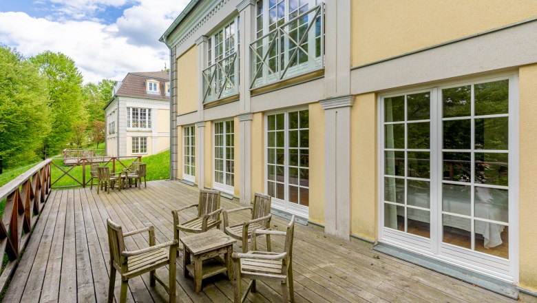 Cavalier houses, © Wiener Alpen / Christian Kremsl Wooden terrace with chairs in front of a yellow building with large windows.