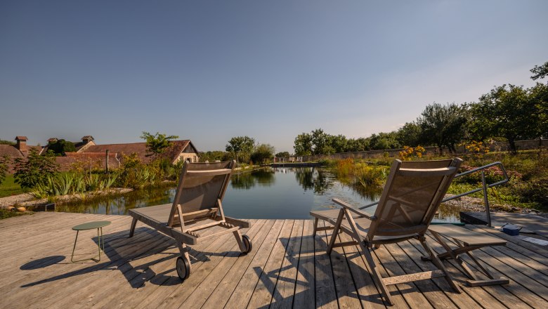 Oberstockstall Estate, © Niederösterreich Werbung / Maximilian Pawlikowsky Two deckchairs on a wooden deck by the pond with garden in the background.