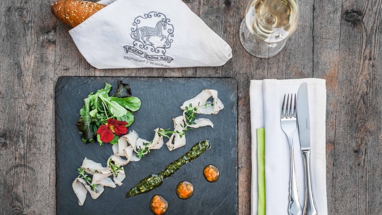 Appetizer, © Martina Siebenhandl Elegant starter on a slate plate with bread, cutlery and wine glass on a wooden table.