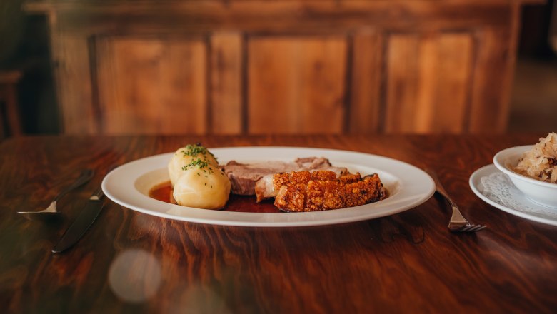 Crust roast, © Niederösterreich Werbung/Daniela Führer Traditional dish with roast pork and dumplings on a wooden table.
