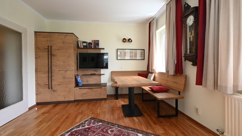 Living room, © Christine Kuppelwieser Cozy living room with wooden furniture, a carpet, a corner bench and a wall clock.