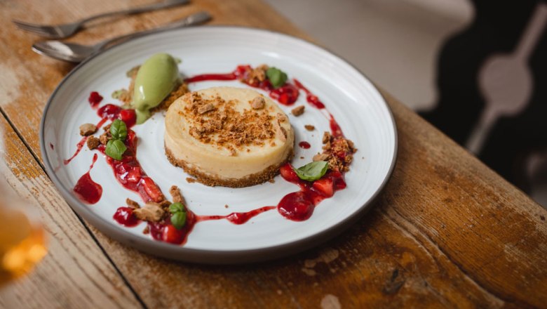 Cheescake, © Niederösterreich Werbung/Daniela Führer A plate with a cheesecake, decorated with red berries and green ice cream, on a wooden table.