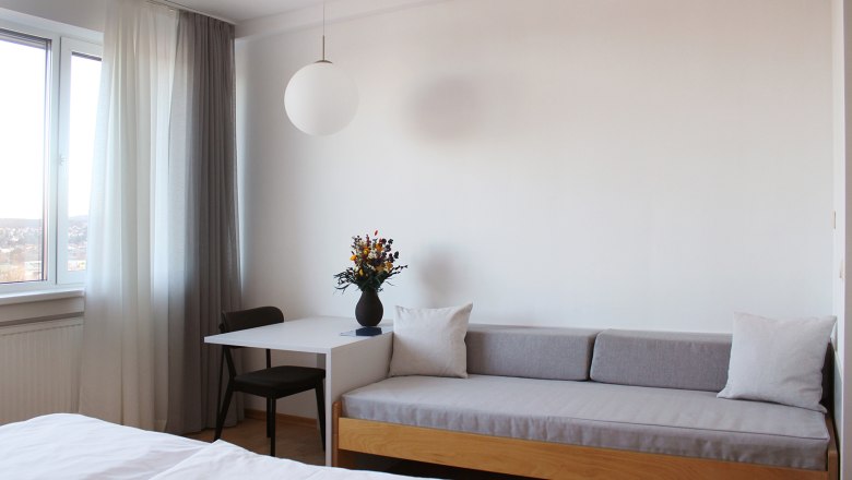 Guest room, © Stadthotel Hollabrunn Modern guest room with sofa, table, chair and window with curtains.