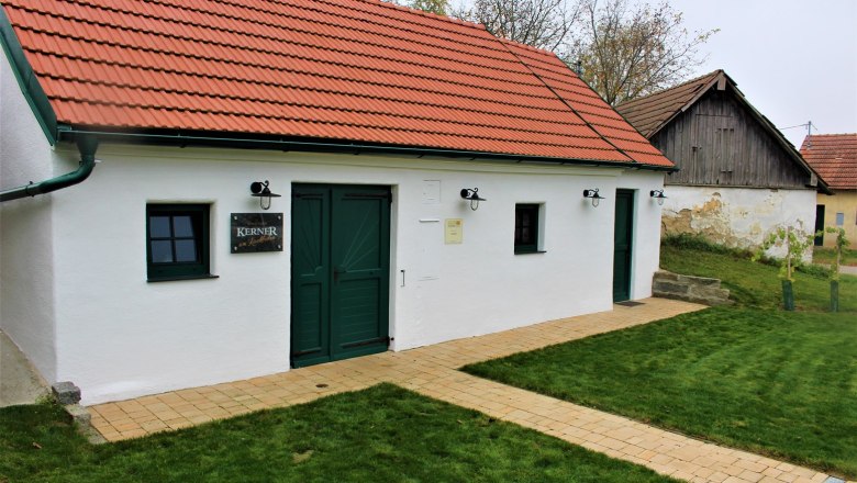 Wine shop, © Weingut Kerner White building with a red roof and green doors, surrounded by lawn.