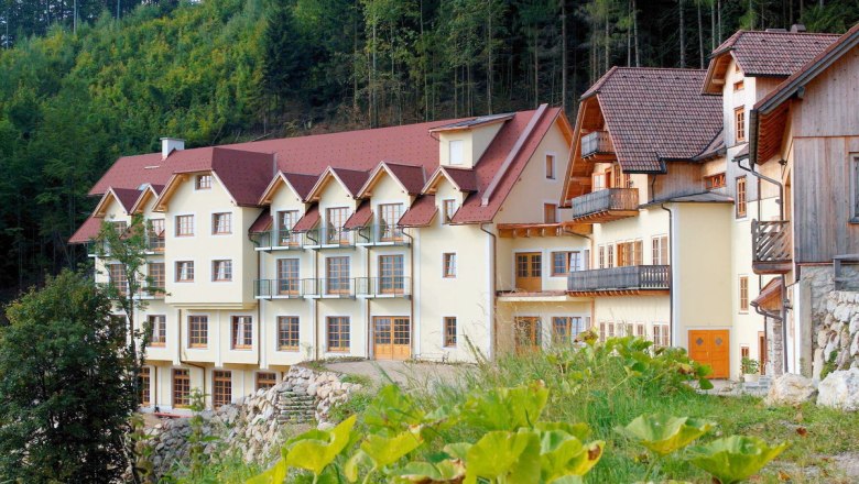 Steinschaler Dörfl, © Steinschaler Dörfl A large, multi-storey building with red roofs and balconies, surrounded by forest.