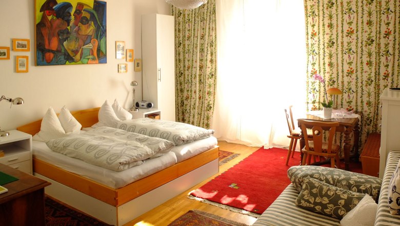 Room example, © Fam. Probst Cozy bedroom with double bed, colorful painting, curtains with floral pattern and small table with chairs.