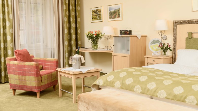 Details in the room of the Hotel-Restaurant Zur Post, © BOW Rita Newman Cozy hotel room with green carpet, red armchair, table with champagne cooler, flowers and bed with green throw.