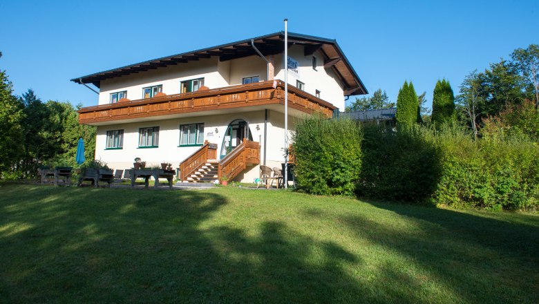 View to the entrance, © Dorfschmiede eG Two-storey house with wooden veranda and garden.