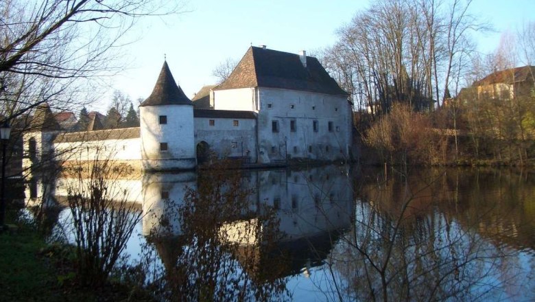Kirchstetten, © Kirchstetten A historic building with towers is reflected in a calm body of water surrounded by bare trees.