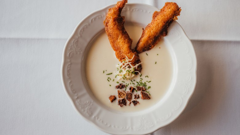 Cream of horseradish soup with smoked trout strips, © Niederösterreich Werbung/Daniela Führer Creamy soup with smoked trout strips and herbs on a white plate.