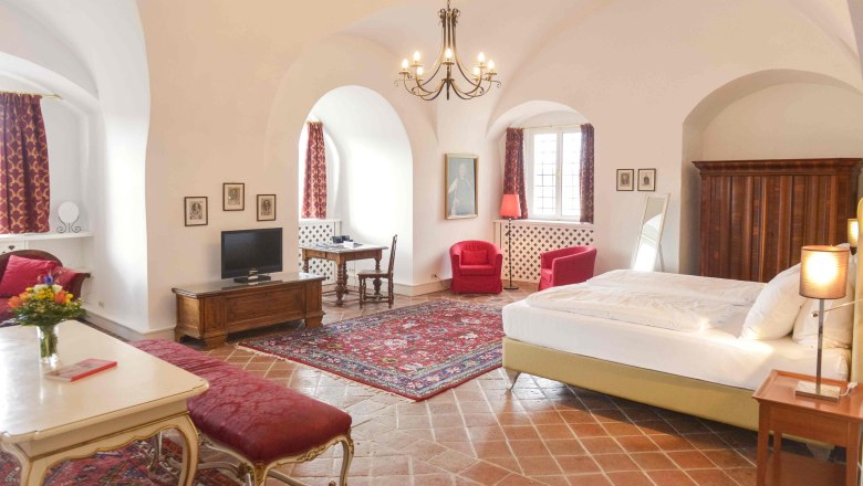 Luxury suite, © Schlosshotel Mailberg / point of view Luxurious suite with antique furniture, red carpets and curtains, a large bed and a chandelier.