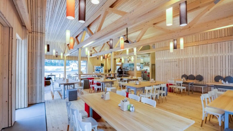 Ötscher-Base Wienerbruck, © Fred Lindmoser Interior view of a modern restaurant with wooden furniture and colorful hanging lamps.