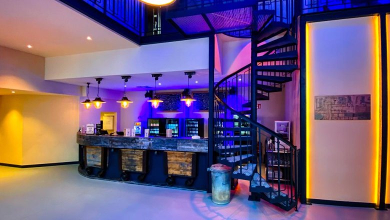 Bar - Paper Mill Variety, © Manfred Sebek Interior view of a bar with spiral staircase and blue lighting.