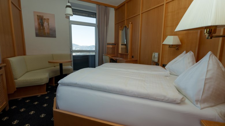 Double room, © Sporthotel Semmering A cozy double room with wooden furniture, a double bed, a seating area and a balcony with mountain views.