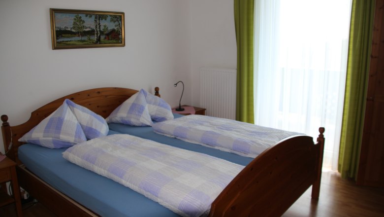 Double room, © Karl Buchner Double room with wooden bed, blue and white checkered bed linen, picture on the wall and green curtain.