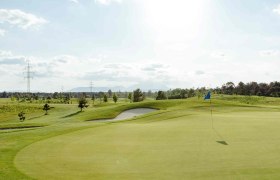gclinsberg2023-328, © Lukas Kucera Golf course with flag on the green, surrounded by trees and electricity pylons under a cloudy sky.