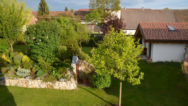 Garden, © Familie Herrmann A well-kept garden with trees, shrubs and a small building with a tiled roof.