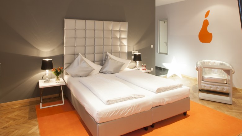 Premium bon-vivant rooms Gürtler, © Stefan Badegruber Modern hotel room with double bed, orange wall decoration and stylish armchair.