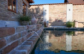 Mediterranean flair in the Weinviertel, © Michaela Wannemacher Brick wall with gargoyles and plants at the edge of a pool.