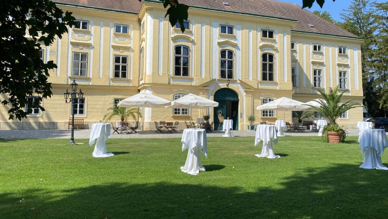 Event castle Margarethen am Moos, © Veranstaltungsschloss Margarethen am Moos Exterior view of the castle, in the foreground a meadow with white bar tables and white parasols