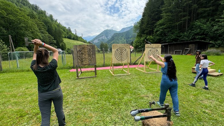 Axe throwing Wilderness Center Nasswald, © Georg Bergthaler People throw axes at outdoor targets surrounded by forest and mountains.