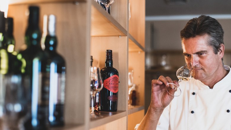 Anton Hiesinger, © Niederösterreich Werbung/David Schreiber A man in a chef's jacket smells a glass of wine in front of a shelf of bottles.
