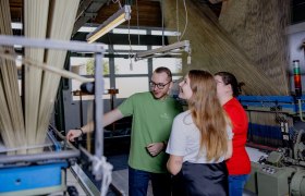 Guided tour through the production, © Waldviertel Tourismus, Matthias Streibel Three people in a textile factory look at a machine.
