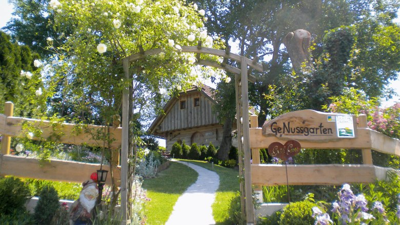 Nut garden, © Nussbaumerhof/Josef Streißelberger Entrance to a garden with wooden gate and 'GeNussgarten' sign.