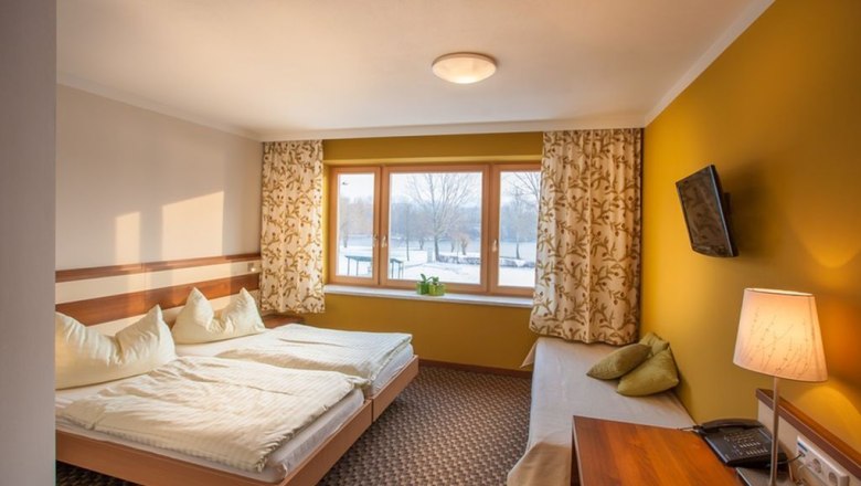Double room 2, © Johann Gruber A cozy double room with two beds, yellow walls, a window with curtains, a TV on the wall and a table lamp.