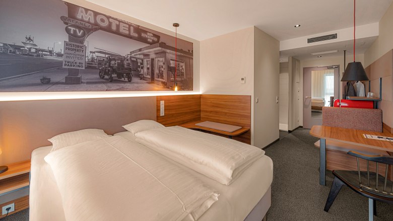 Zündwerk Motel, © propertyphotos.at Modern hotel room with double bed, mural of an old motel, wooden furniture and desk.