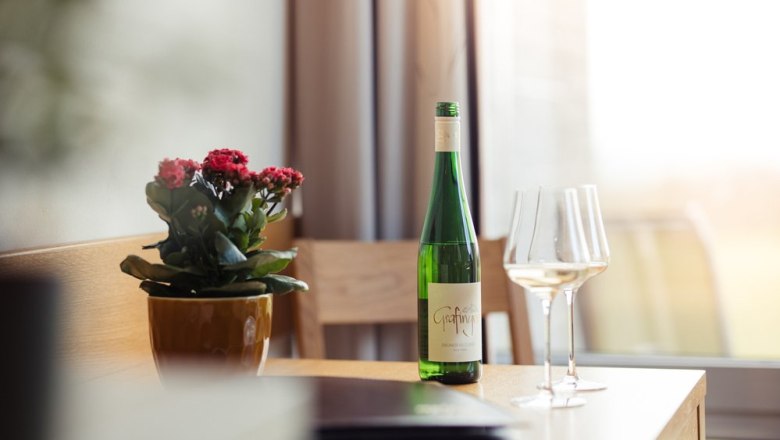 Vinophile living., © Weingut & Weinblick Grafinger Wine bottle and glasses on a table next to a potted plant.