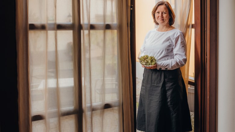 Hostess Karin Rosenberger looks after the guests, © Niederösterreich Werbung/Daniela Führer A woman stands in a doorway holding a bowl of salad.