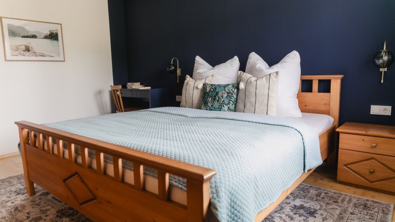 Bedroom vacation nest Zehetbauer, © heiter-weiter.at/Karl Stangl Cozy bedroom with wooden bed, blue wall and decorative pillows.