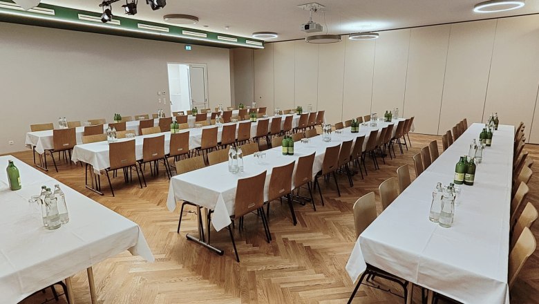 The GrimmenStein Kulmriegelsaal, © Das GrimmenStein Large hall with wooden chairs, long tables, white tablecloths and drinks bottles.