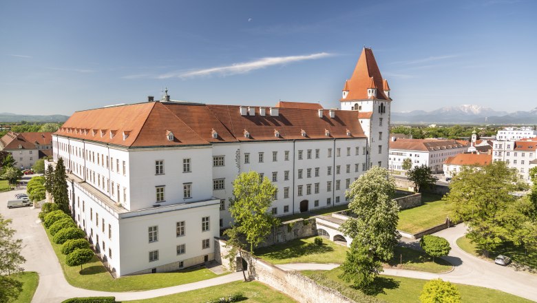 Military academy seen from Eleonorenweg, © Wiener Alpen, Foto: Franz Zwickl View of a historic military academy with a red roof and tower, surrounded by green trees and lawns, mountains in the background.