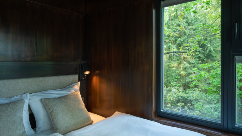 edelførst tree houses, © Robert Tober Interior view of a tree house with a bed and a window overlooking the forest.
