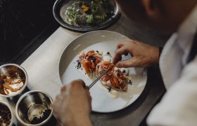 Cuisine: bold, wild, rooted in the region, © Niederösterreich Werbung/Sophie Menegaldo Chef decorates a dish with salmon and vegetables on a plate.