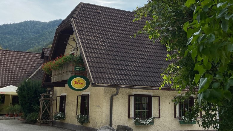 Gasthof Brandstätterhof, © Wiener Alpen Traditional inn with flowers and Murauer sign, surrounded by trees.