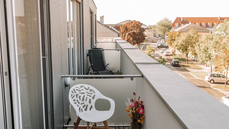 Business terrace HEINhotel vienna airport, © HEINhotel vienna airport Balcony with white chair and bouquet of flowers, view of the street and building.