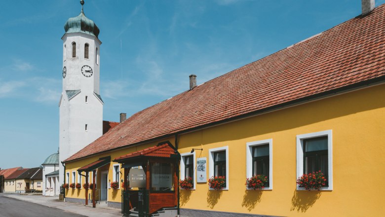 Pub with excellent spirits, © Niederösterreich Werbung/David Schreiber Yellow building with church tower and blue sky in a cityscape.