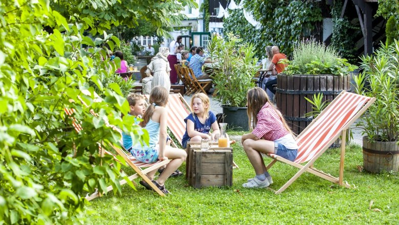Gebeshuber, © Gebeshuber Children sit on deckchairs in the garden of a café.
