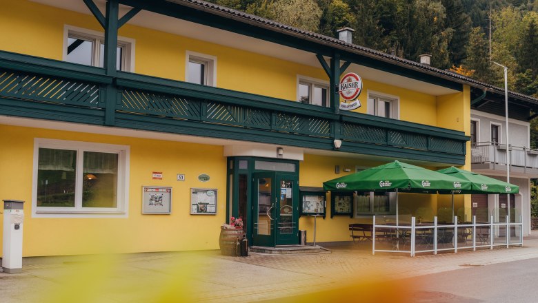 Inn with its own small hydroelectric power station, © Niederösterreich Werbung/Daniela Führer Yellow pub with green awnings and signs, surrounded by trees.