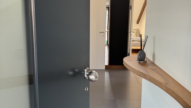 Entrance area, © Juwel am Stadtrand Modern entrance area with open door, tiled floor and wooden shelf on the wall.