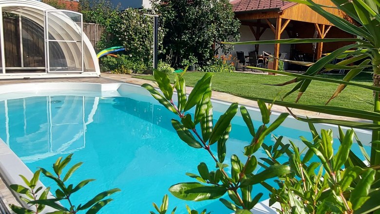 Swimming pool, © Trachsler A private garden with a pool surrounded by plants and a covered seating area.