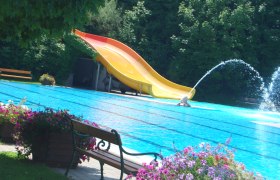 St. Valentin outdoor pool, © zVg Gemeinde St. Valentin An outdoor pool with a yellow slide, water fountain and flowers in the foreground.