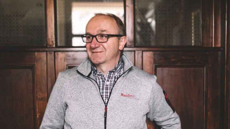 Landlord Leopold Hofbauer, © Niederösterreich Werbung/Mara Hohla A man with glasses and a gray jacket stands in front of a wooden wall.
